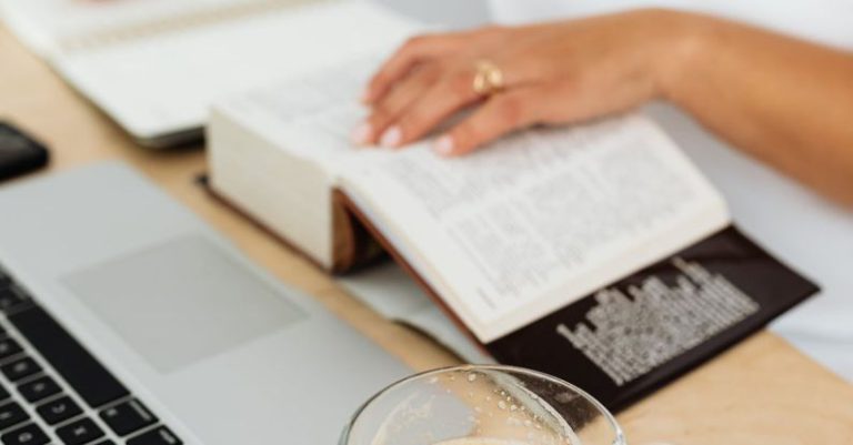 Dictionary Technology - Woman Sitting at the Desk with a Laptop and a Cup of Coffee while Using a Paper Dictionary