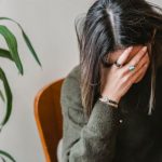 Mistakes Avoidance - Unrecognizable young upset female millennial with dark hair in stylish sweater covering face with hand while siting on chair at home