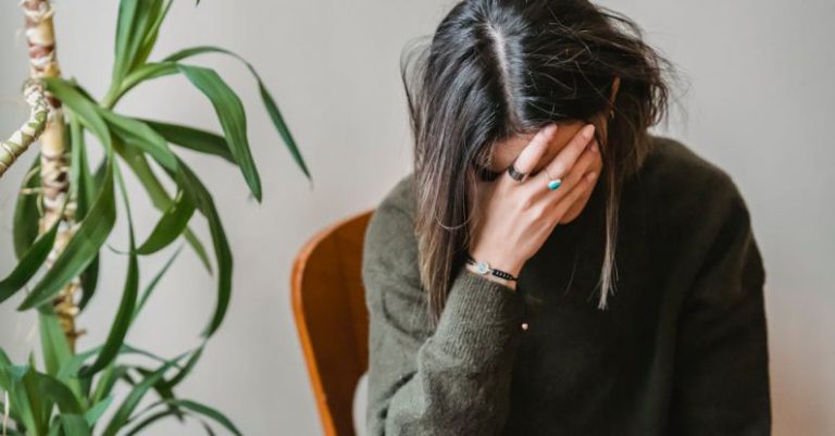 Mistakes Avoidance - Unrecognizable young upset female millennial with dark hair in stylish sweater covering face with hand while siting on chair at home