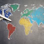 Benchmarking Guide - Top view of crop anonymous person holding toy airplane on colorful world map drawn on chalkboard