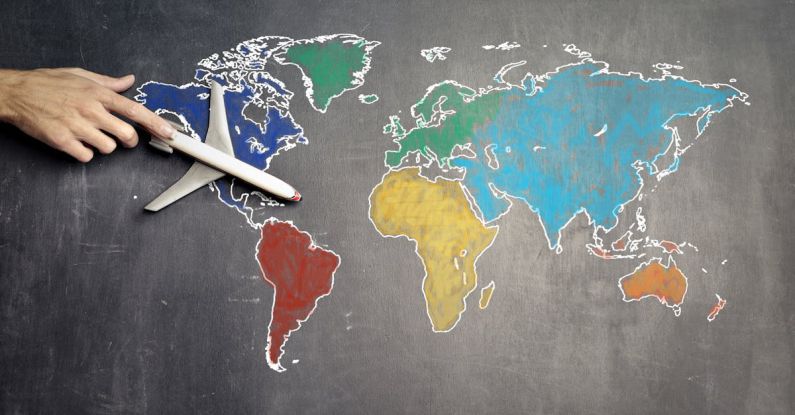 Benchmarking Guide - Top view of crop anonymous person holding toy airplane on colorful world map drawn on chalkboard