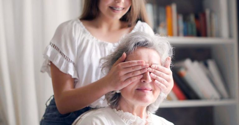 Game Library - Cheerful teenager playing with grandmother guess who game while making surprise in light living room