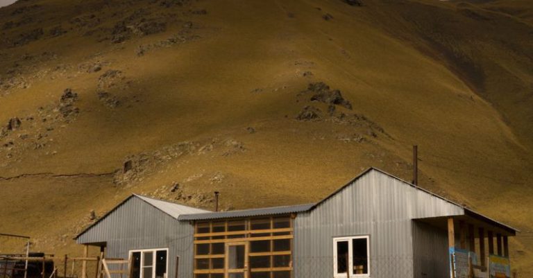 Silent Build - Picturesque view of small rural cottage on grassy terrain near hills under cloudy sky