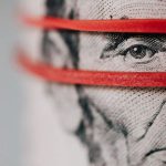 Upgrade Budget - Closeup of rolled United States five dollar bills tightened with red rubber band