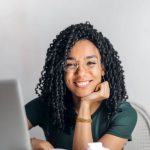 Content Creation Budget - Happy ethnic woman sitting at table with laptop
