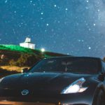 Compact Build - Modern coupe car with glowing headlights parked on asphalt road against bright night sky