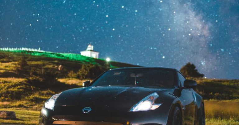 Compact Build - Modern coupe car with glowing headlights parked on asphalt road against bright night sky