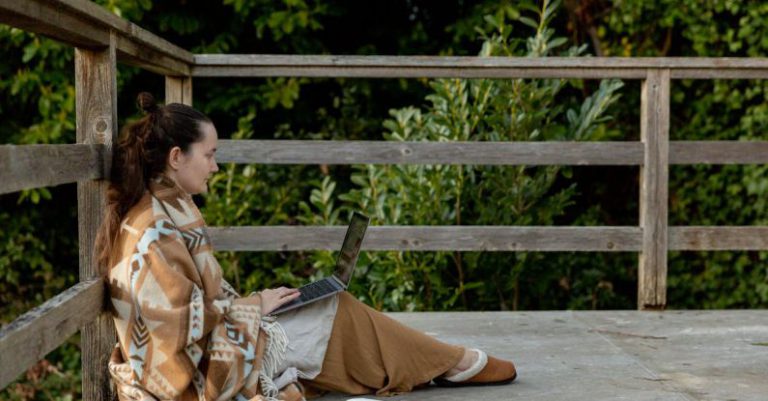 Sleeper PC - Adult focused female blogger sitting on veranda with laptop