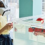 VR Development - Side view of little girl wearing VR goggles and exploring new robot with controllers in light room