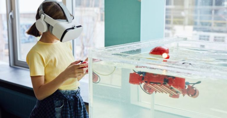 VR Development - Side view of little girl wearing VR goggles and exploring new robot with controllers in light room