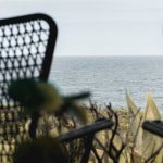 Quiet Luxury - Wooden terrace with wicker armchairs placed nearby lush greenery in front of endless rippling seawater
