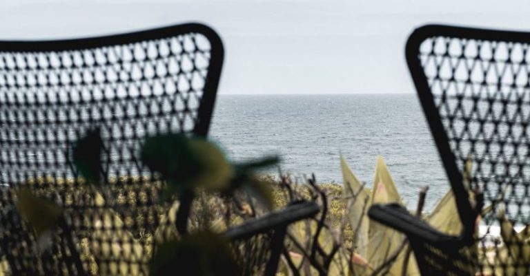 Quiet Luxury - Wooden terrace with wicker armchairs placed nearby lush greenery in front of endless rippling seawater